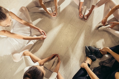 This image shows young ballerinas stretching while seated in a circle. Tailoring your classes to different audiences and genres is one of our top tips for dance studio owners.